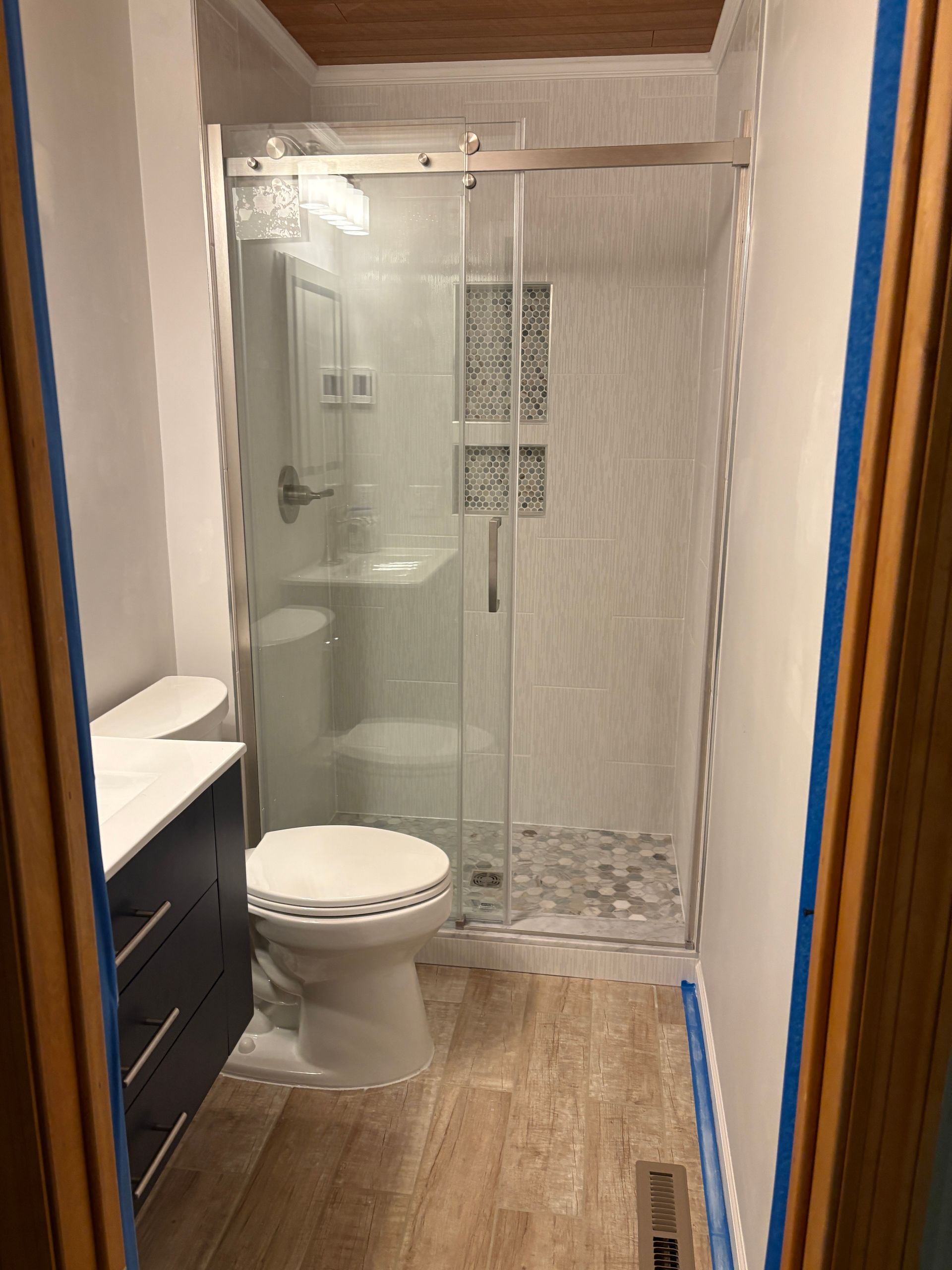 Bathroom with a glass shower, toilet, and vanity. Features light tile, gray and white tones.