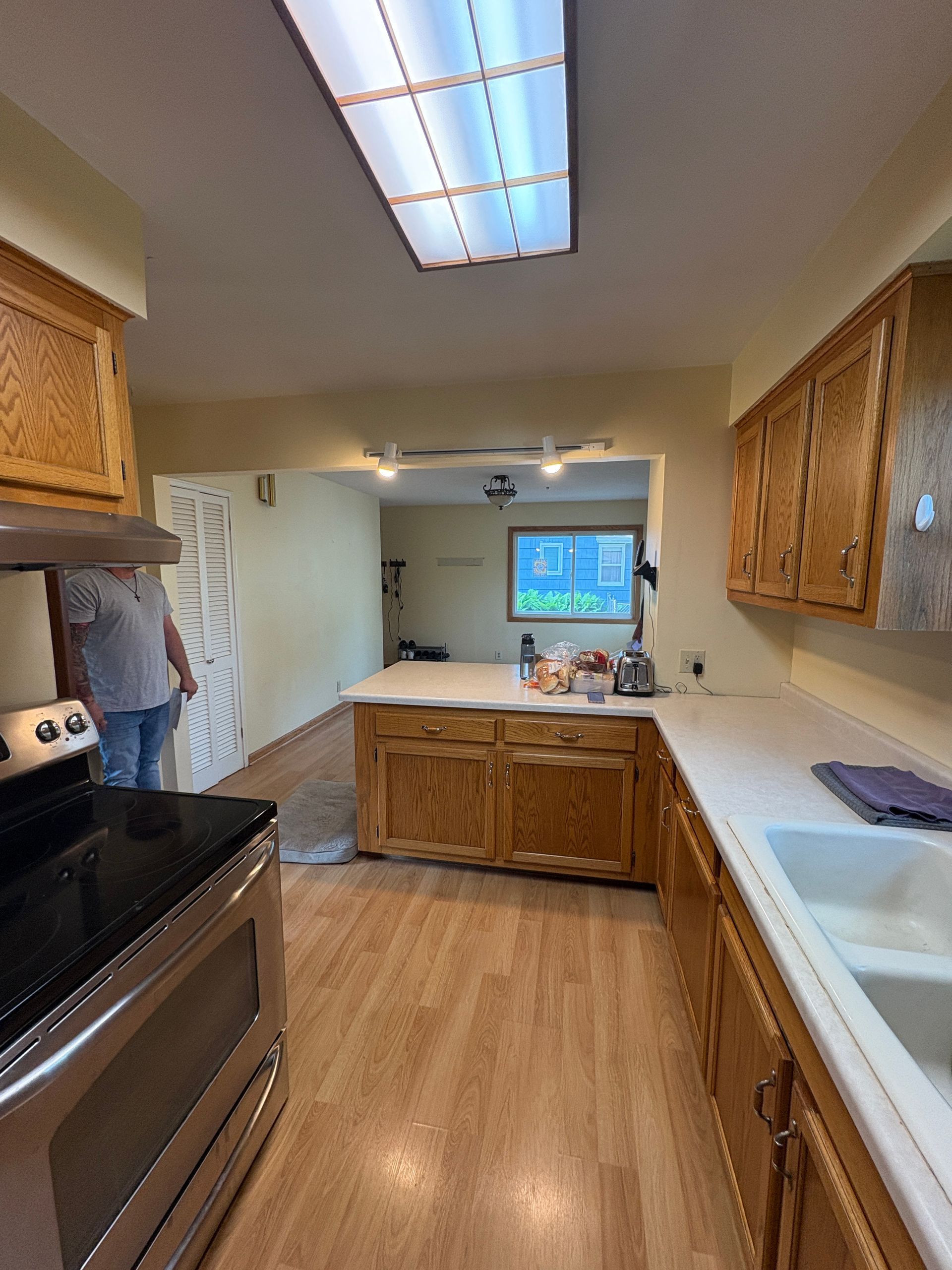 Kitchen with wooden cabinets, island, and appliances. A person stands near a doorway.