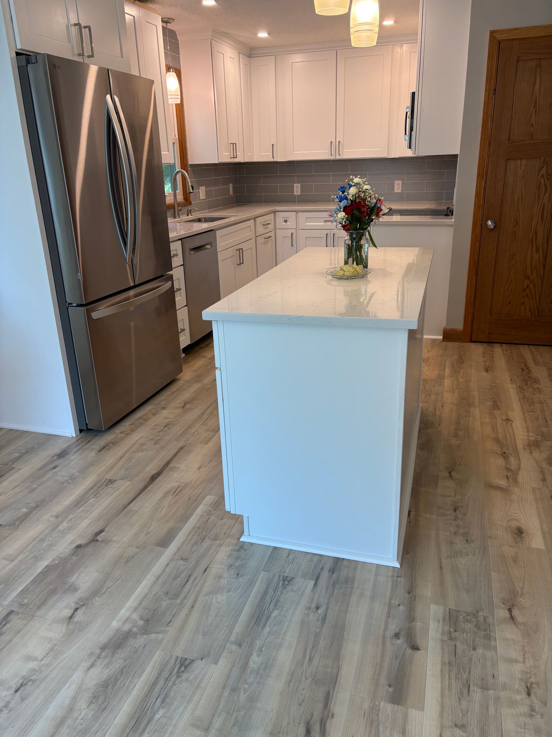 White kitchen with island, stainless steel fridge, light wood floors, and flowers on the island.
