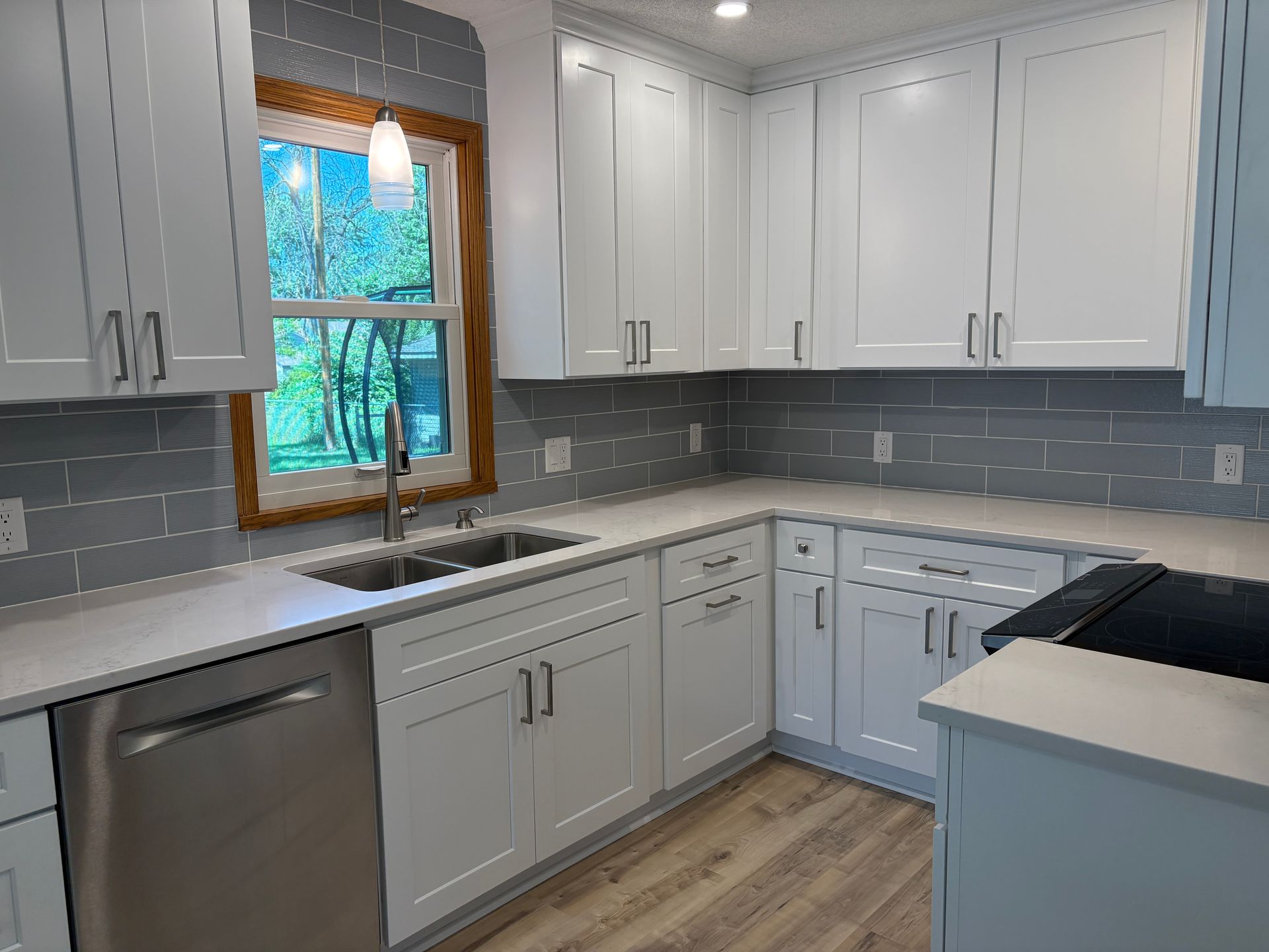 White kitchen cabinets, stainless steel appliances, gray backsplash, and light countertops.