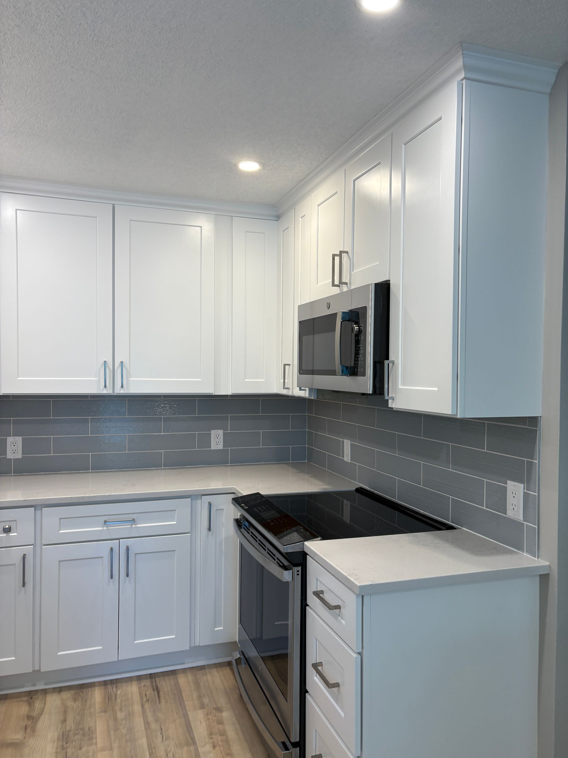 White kitchen with white cabinets, stainless steel appliances, and gray backsplash.