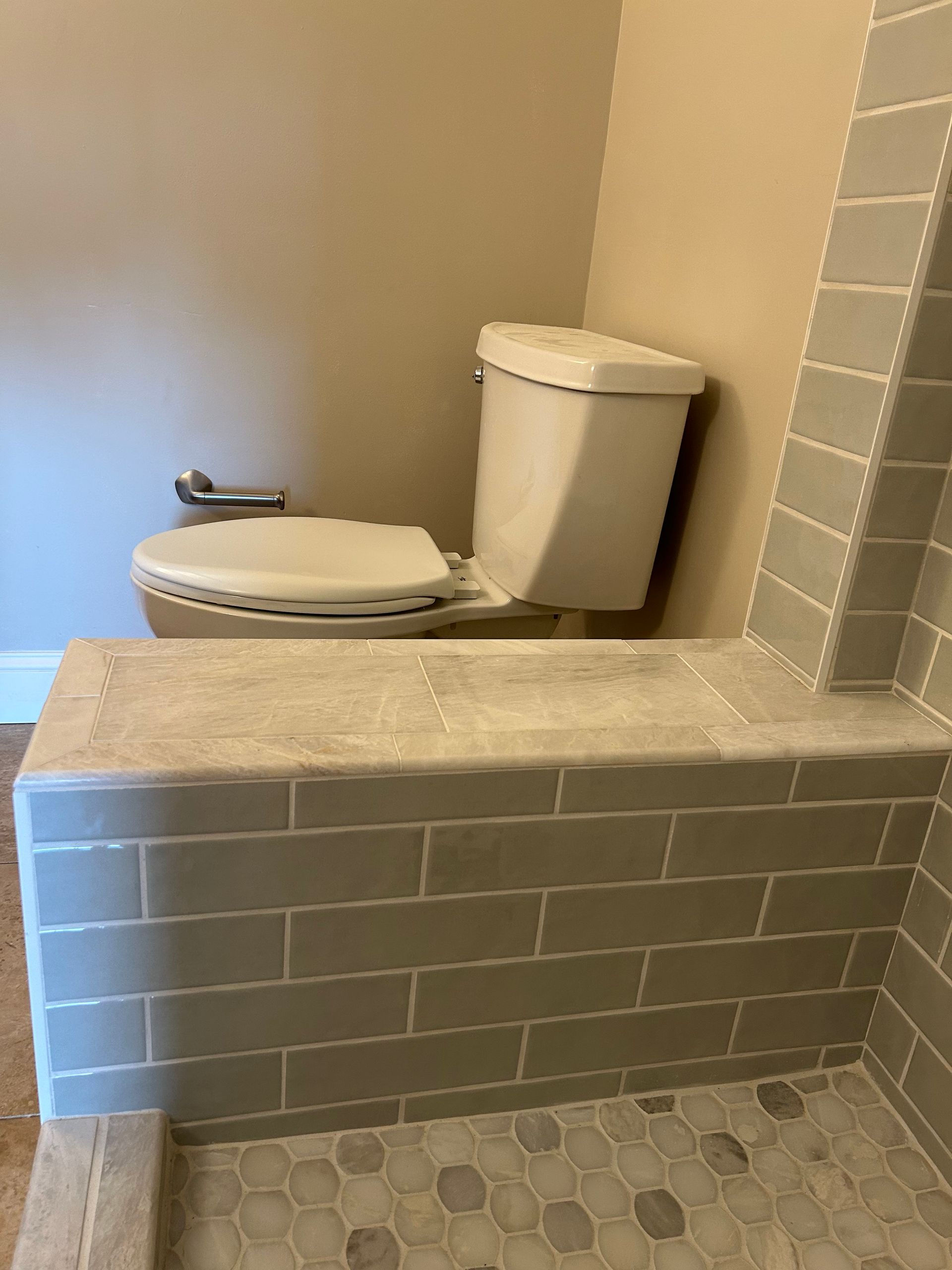 Bathroom with a toilet, shower bench, and gray tile.
