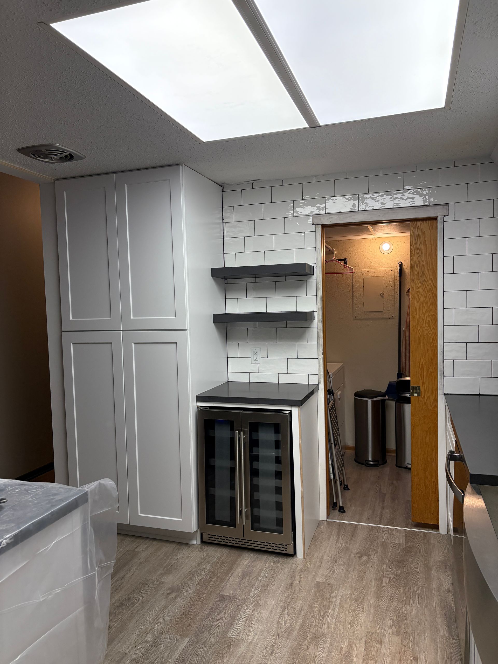 Modern kitchen with white cabinets, wine fridge, open shelving, and textured white tile wall.