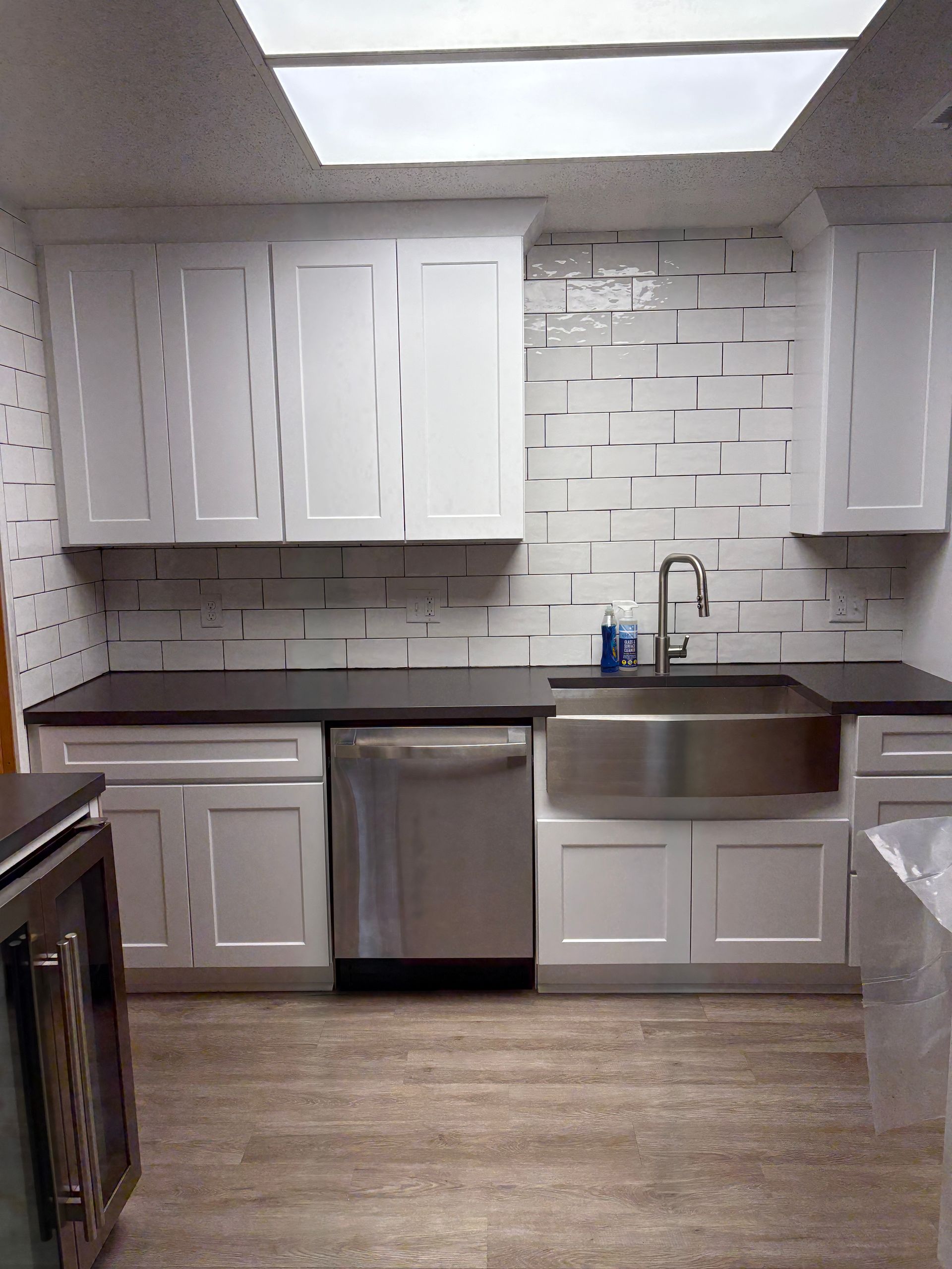 White kitchen with stainless steel appliances, dark countertops, and patterned backsplash.
