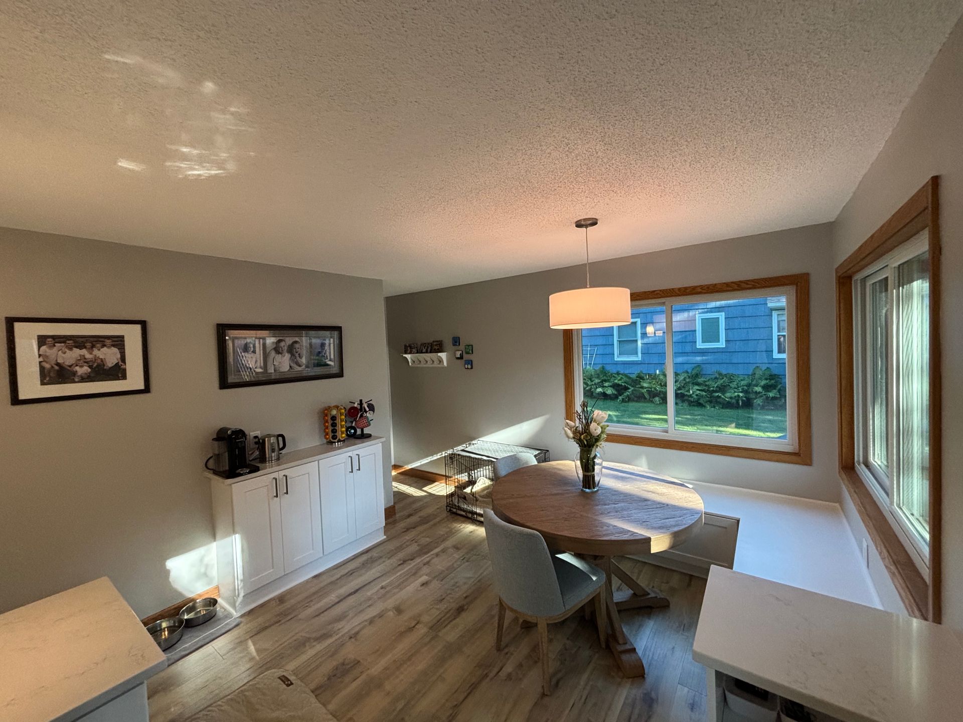 Dining room with round wooden table, light blue chairs, large window, and light wood floors.