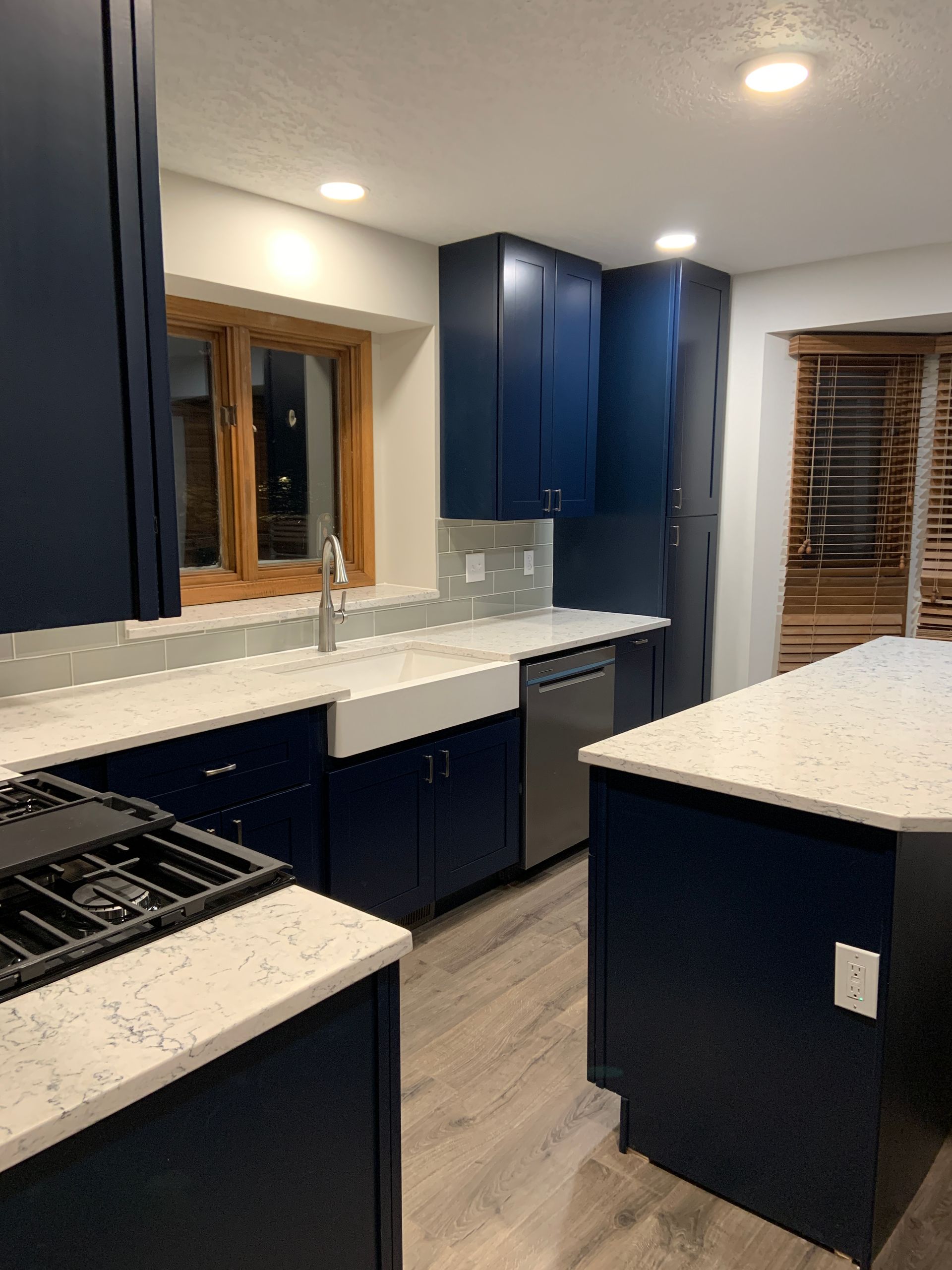 Navy blue kitchen with white countertops and stainless steel appliances.