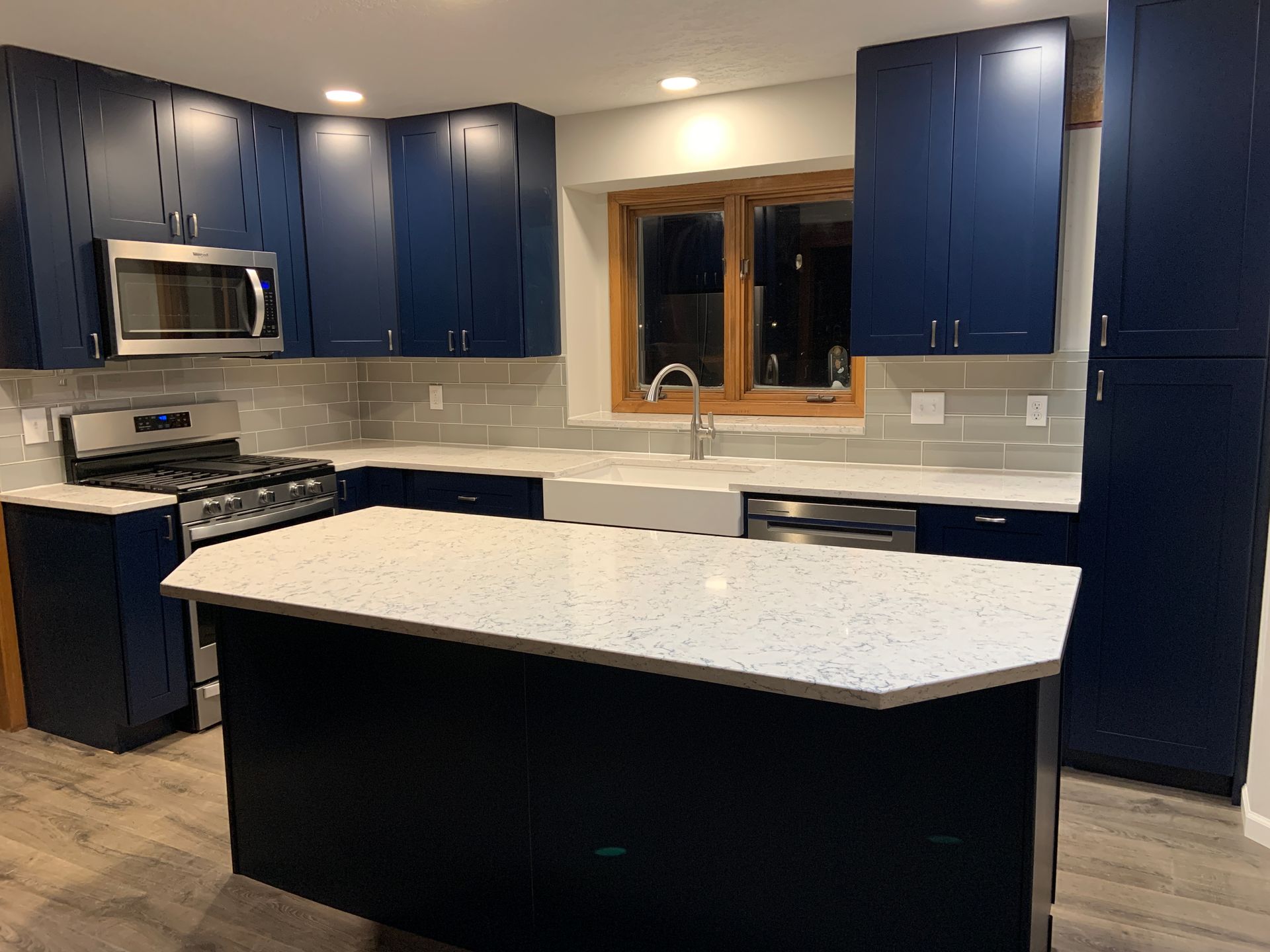 Navy blue kitchen cabinets with a white countertop island. Stainless steel appliances and gray backsplash.