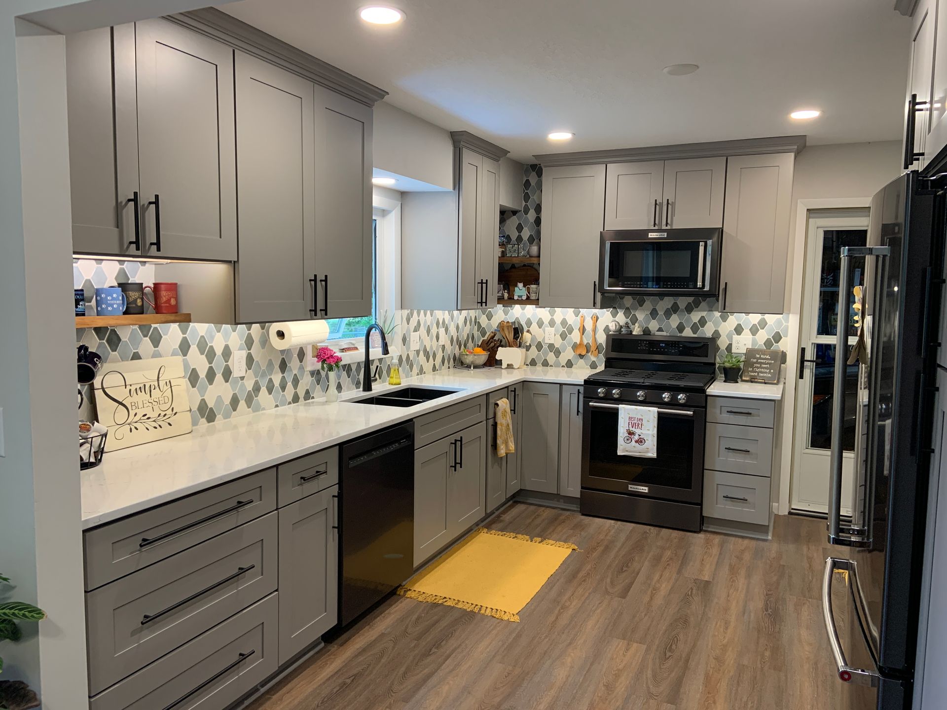 Gray and white kitchen with gray cabinets, black appliances, white countertops, and wood-look flooring.