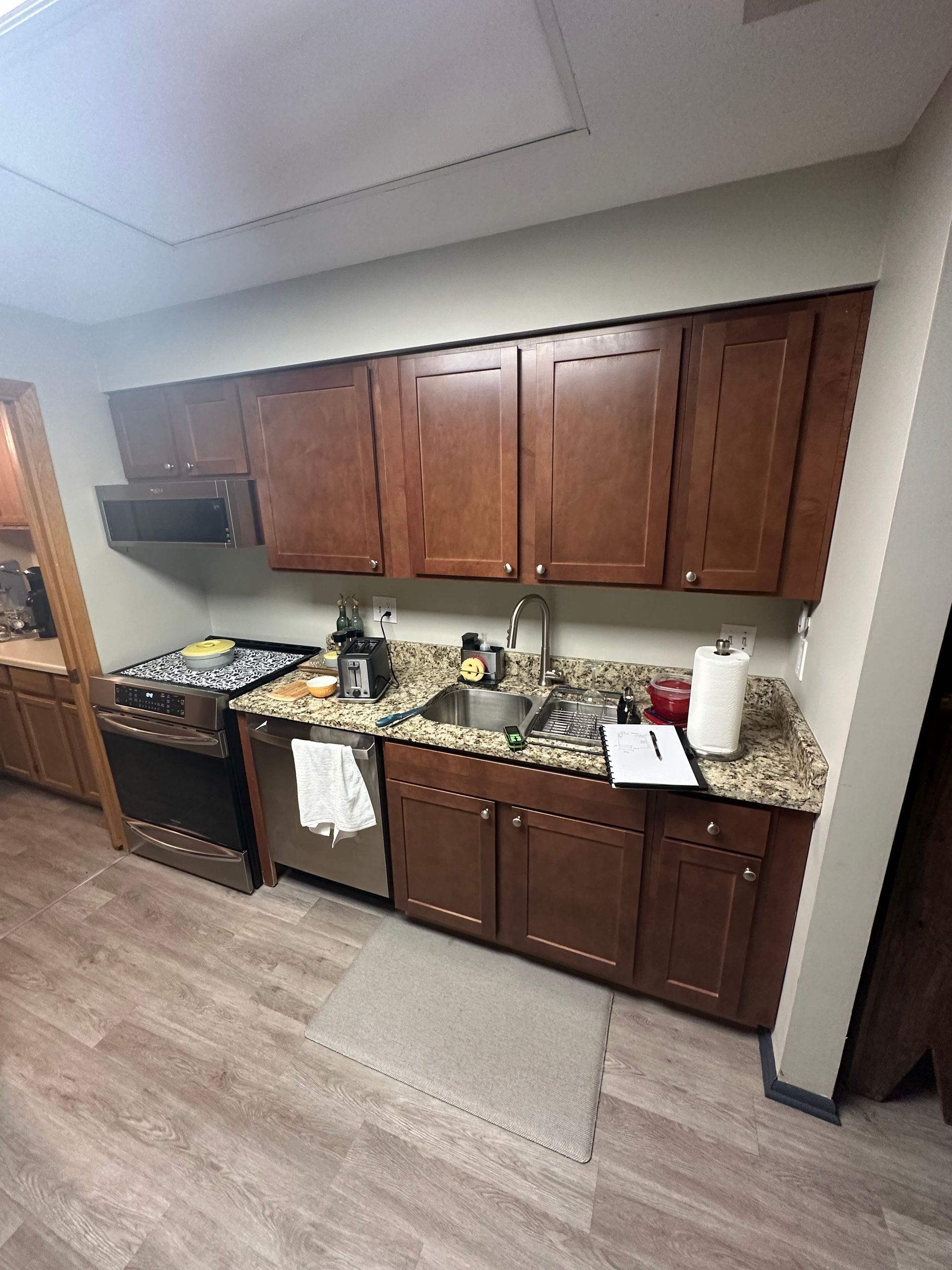 Kitchen with dark brown cabinets, granite countertops, stainless steel sink, and light wood-look flooring.