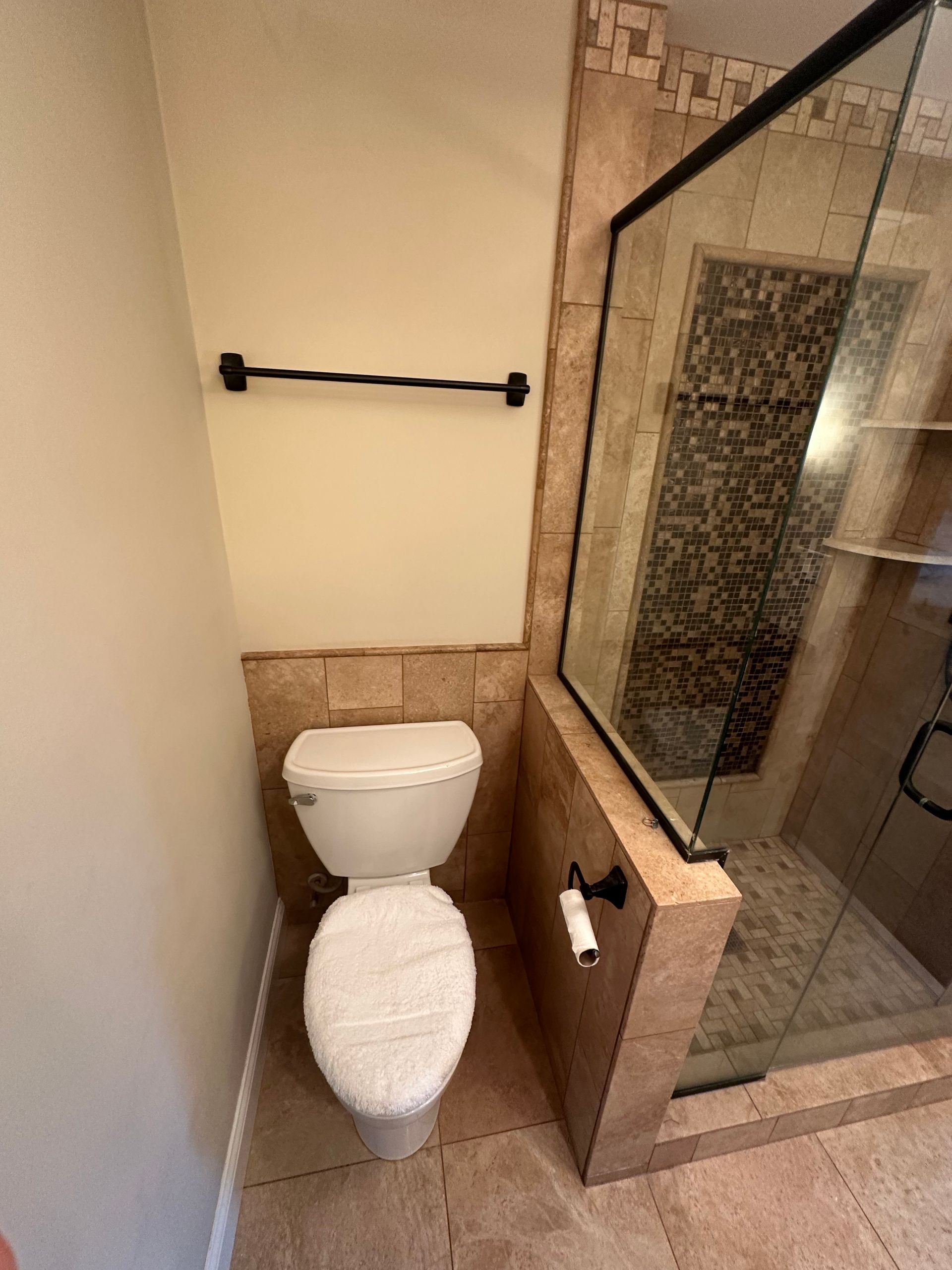 Toilet in a bathroom alcove with a glass shower door and towel rack.