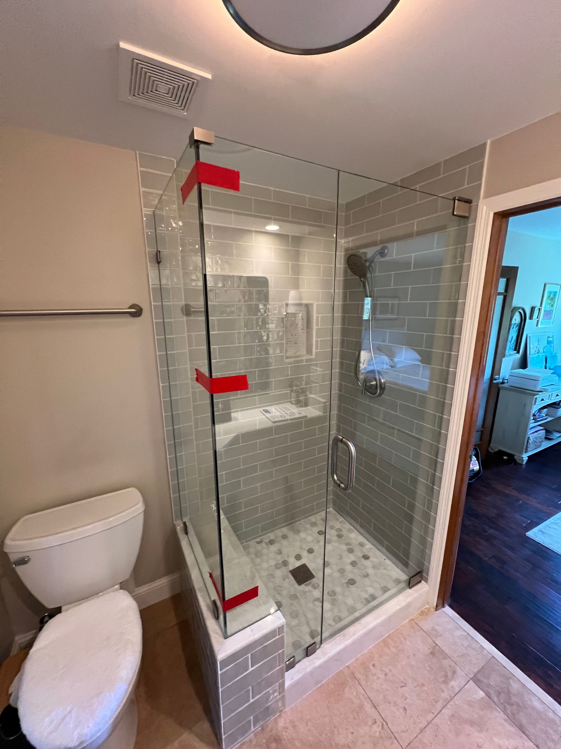 Bathroom with glass shower, toilet, and towel rack. Tan walls, red accents, tile flooring.