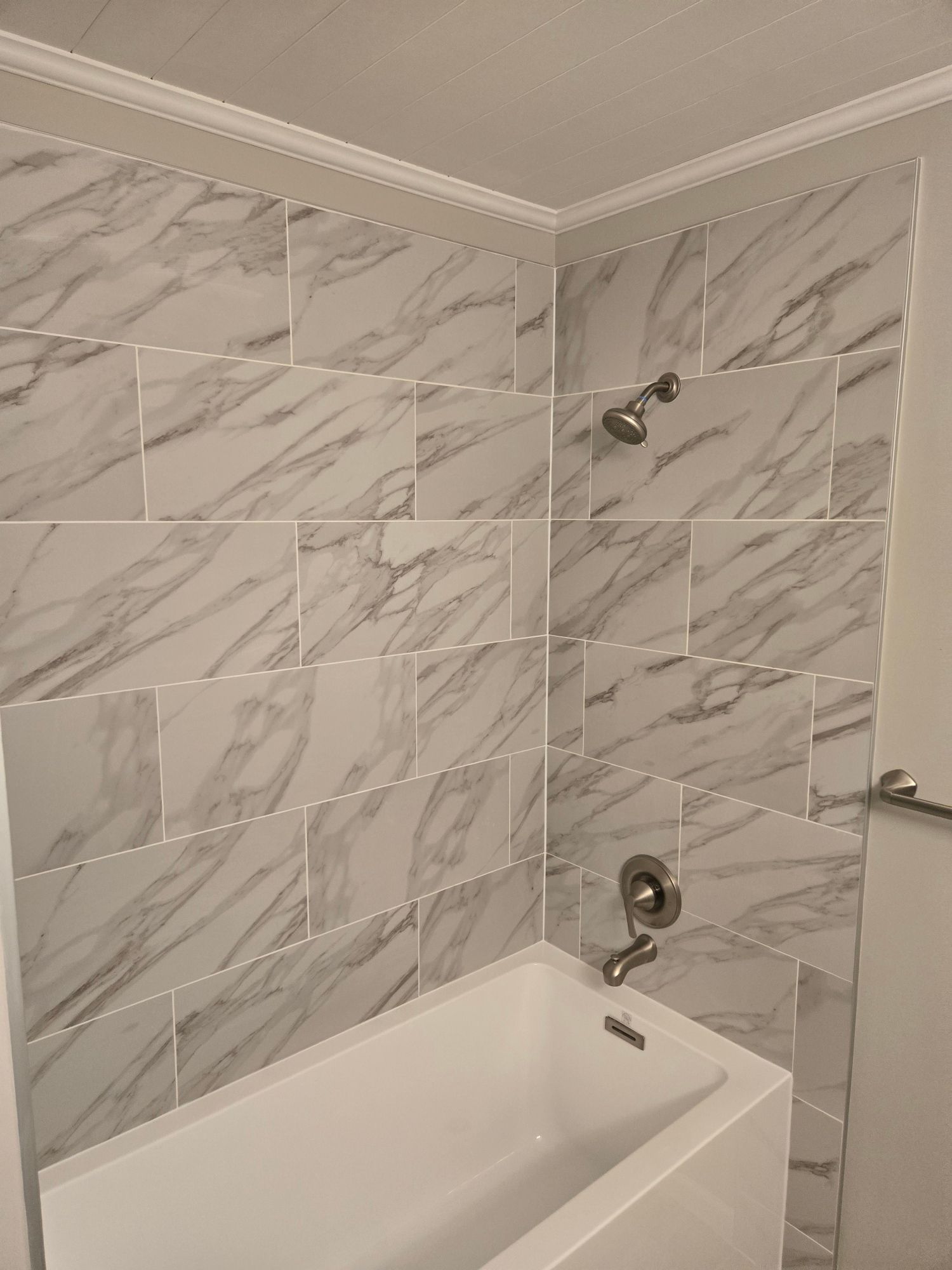 Bathroom corner with white marble-look tiles, showerhead, and bathtub.
