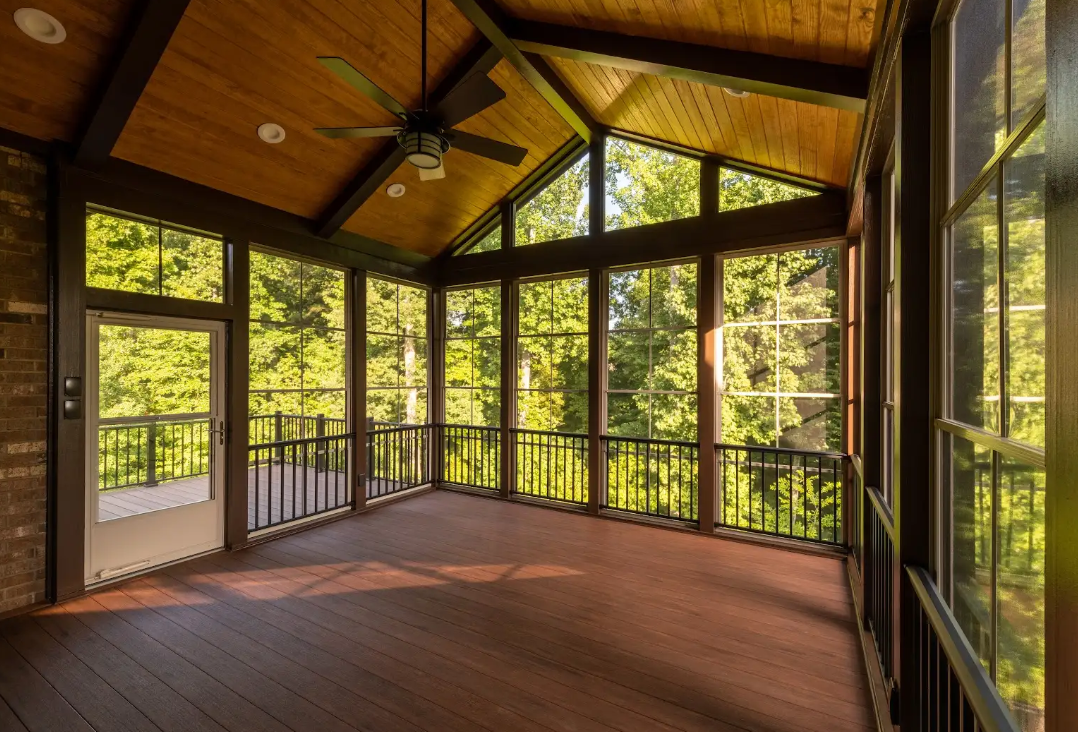 Screened-in porch with brown decking and ceiling, large windows looking out onto a bright green forest.