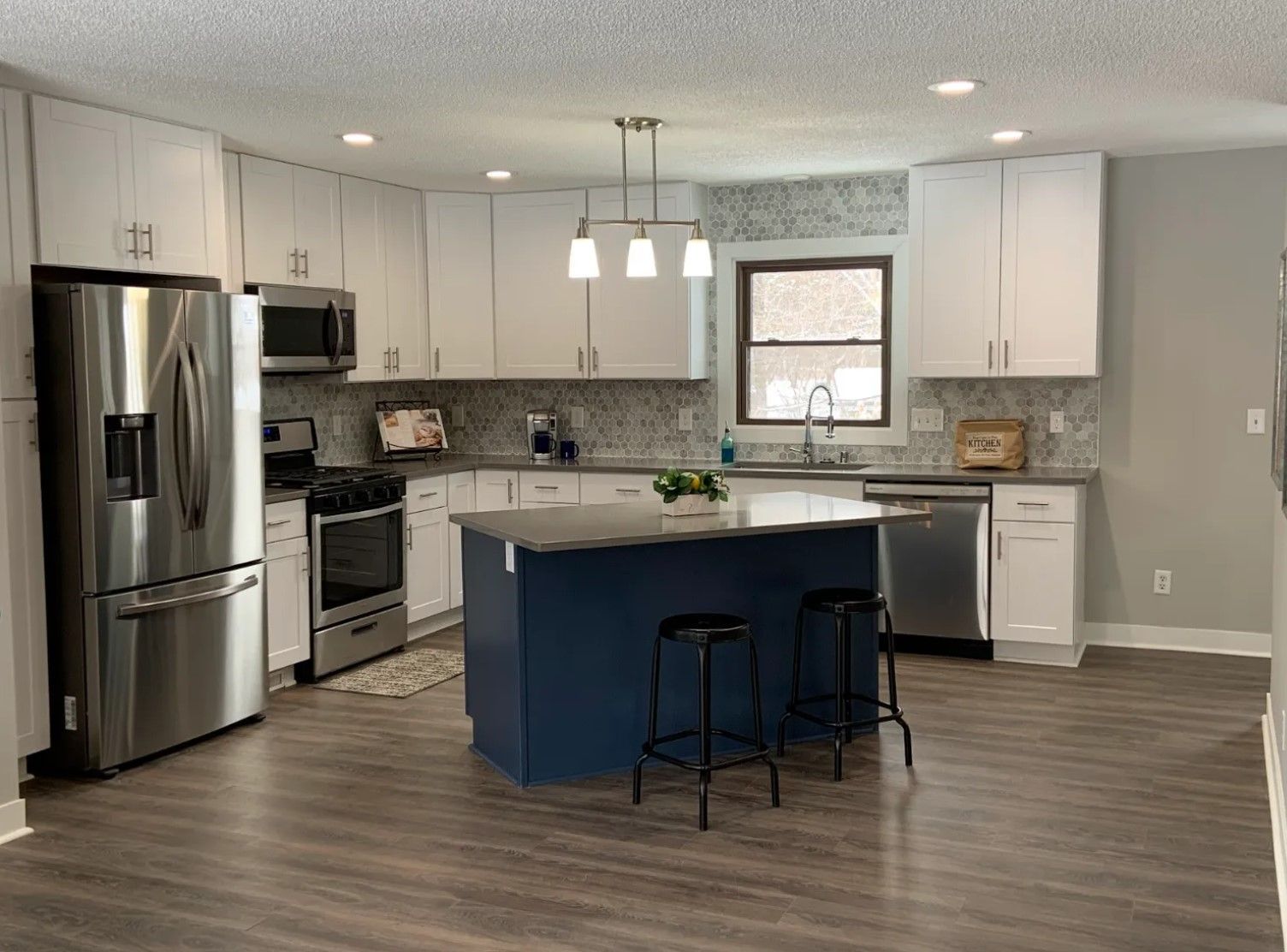 Modern kitchen with white cabinets, blue island, stainless steel appliances, and dark wood flooring.