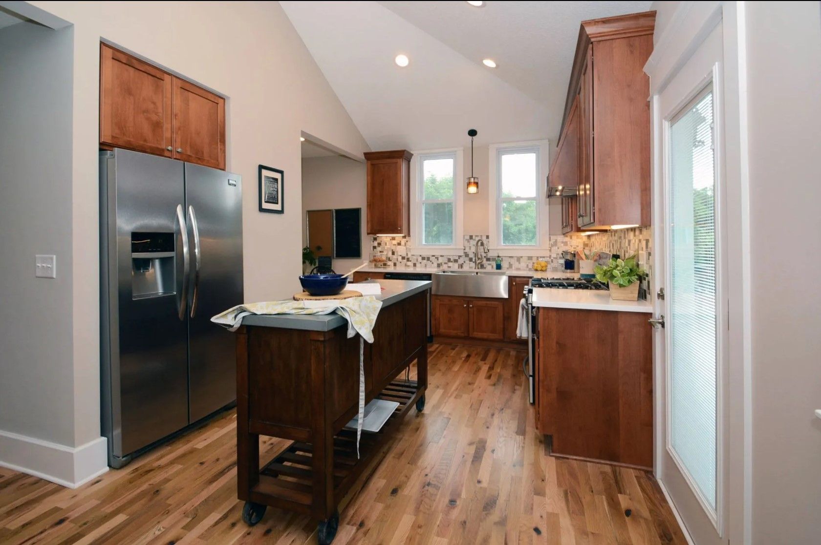 Kitchen with wooden cabinets, stainless steel refrigerator, island, and wood floor.