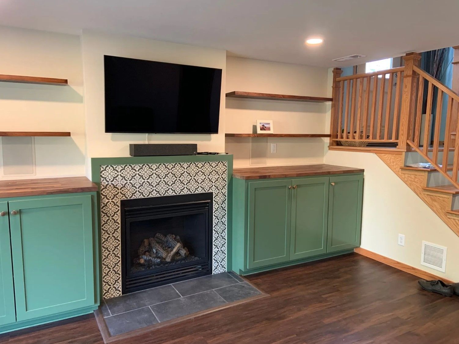Green cabinetry, fireplace, and shelves in a living room; a TV hangs above the fireplace.