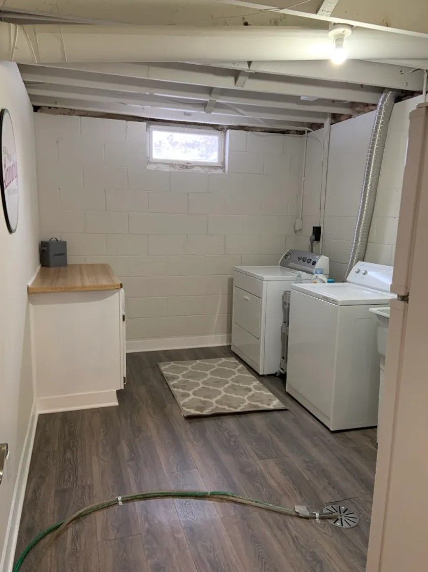 Laundry room with white appliances, gray rug, wood-look flooring, and a small window.