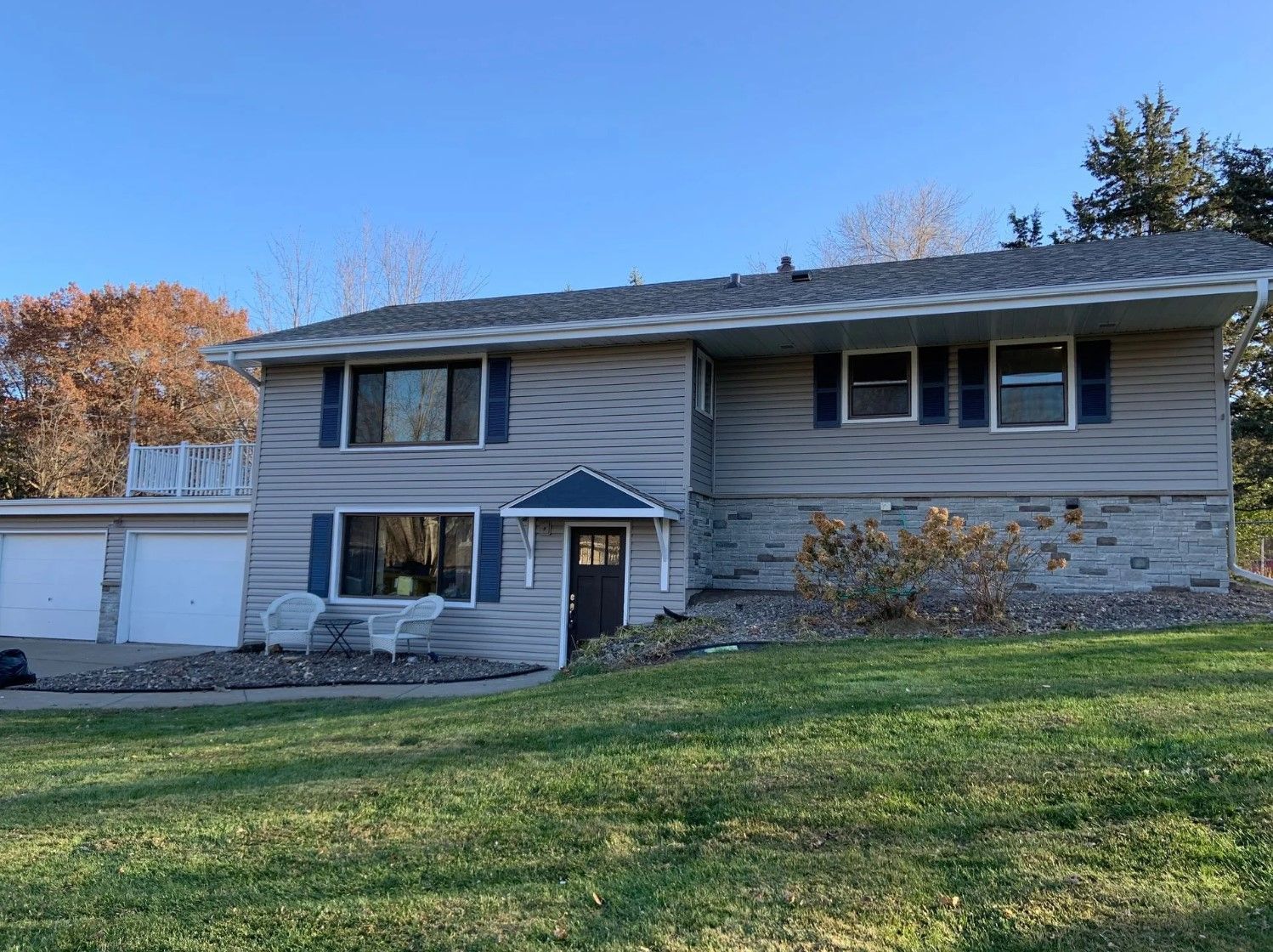 Two-story house with gray siding, blue shutters, and attached garage on a grassy lot under a blue sky.