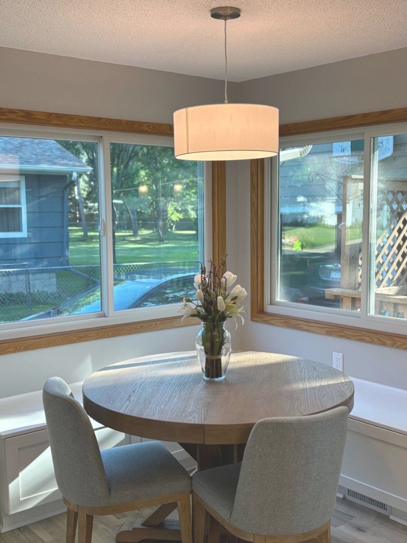 Dining area with round table, chairs, and pendant light fixture. Windows with outdoor view.