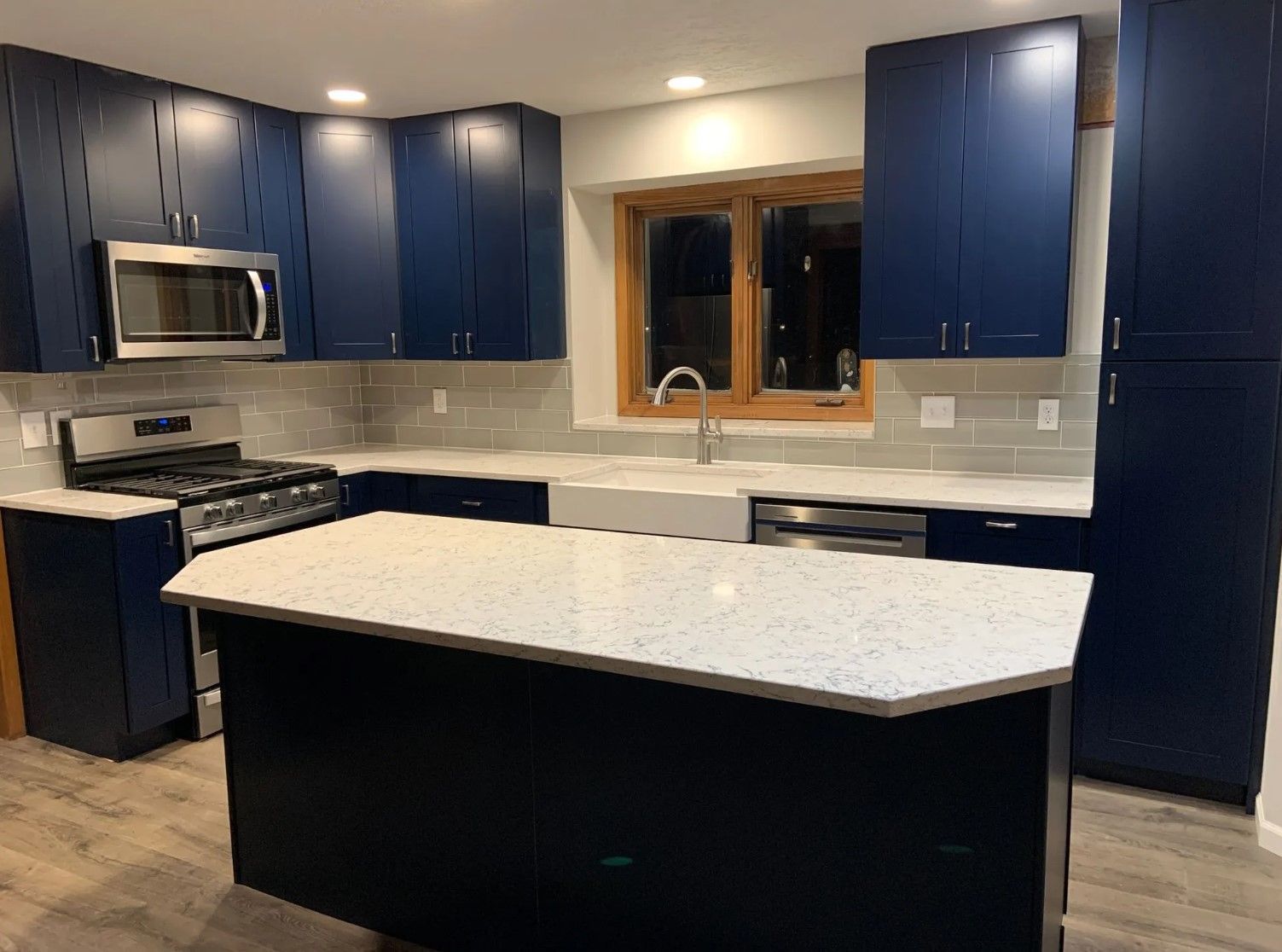 Blue kitchen cabinets with white countertop and island. Stainless steel appliances.