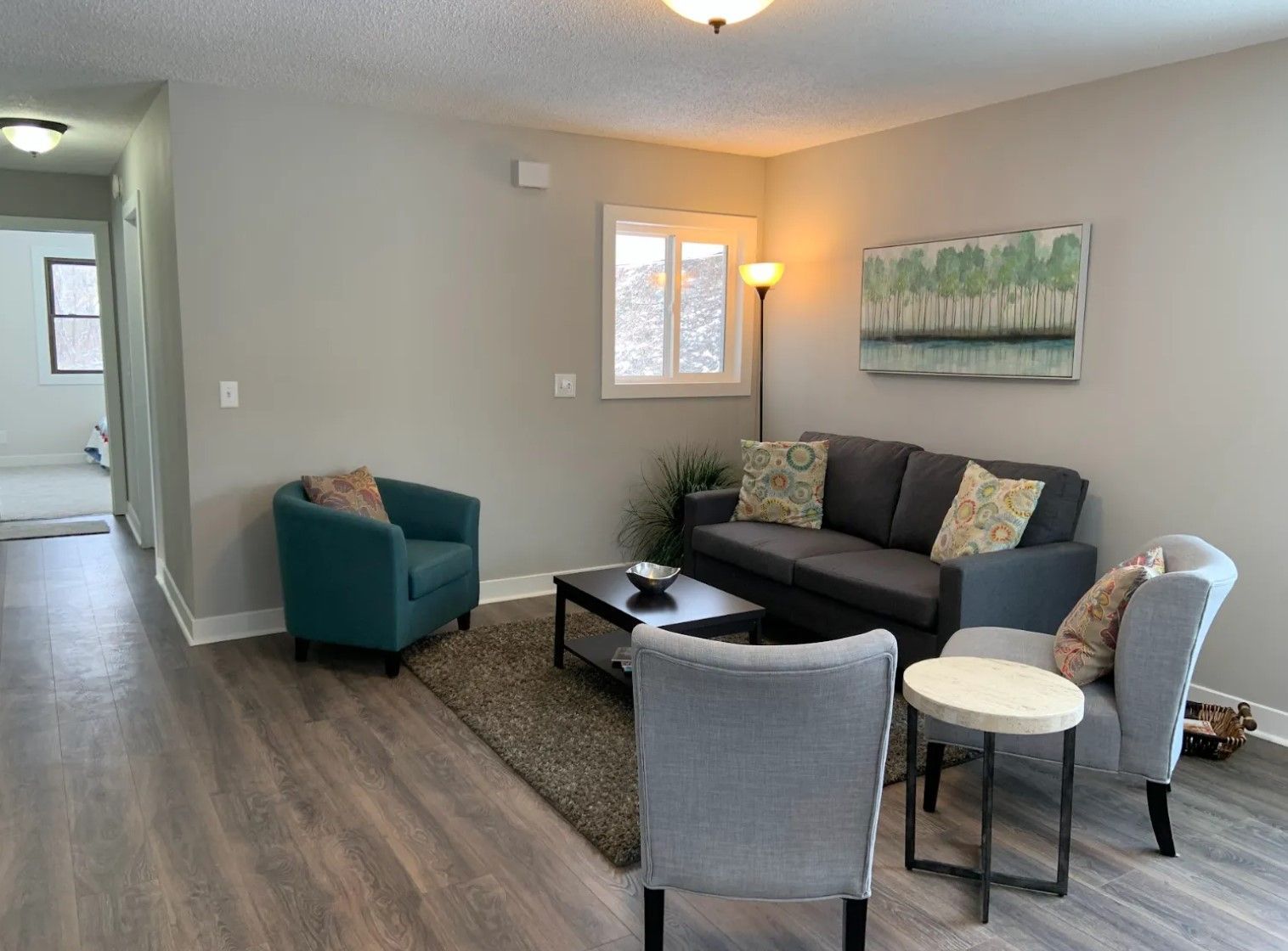 Living room with grey walls, dark grey sofa, teal armchair, and grey chairs around a black coffee table.