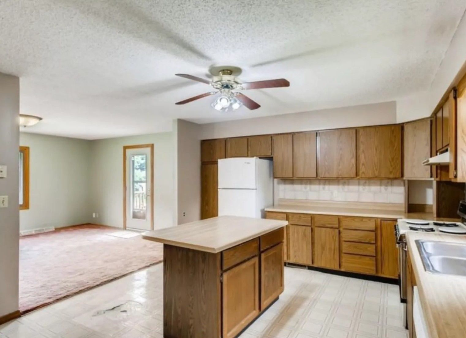 Kitchen with light-colored cabinets, white refrigerator, and an island. A ceiling fan hangs above.
