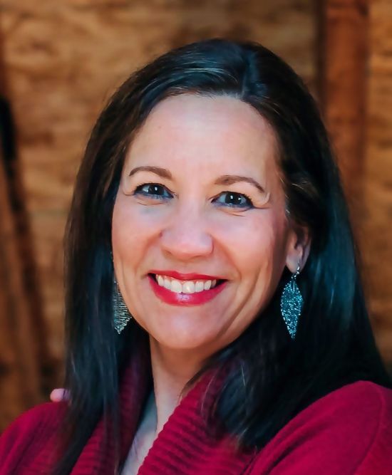 A woman wearing a red sweater and earrings smiles for the camera