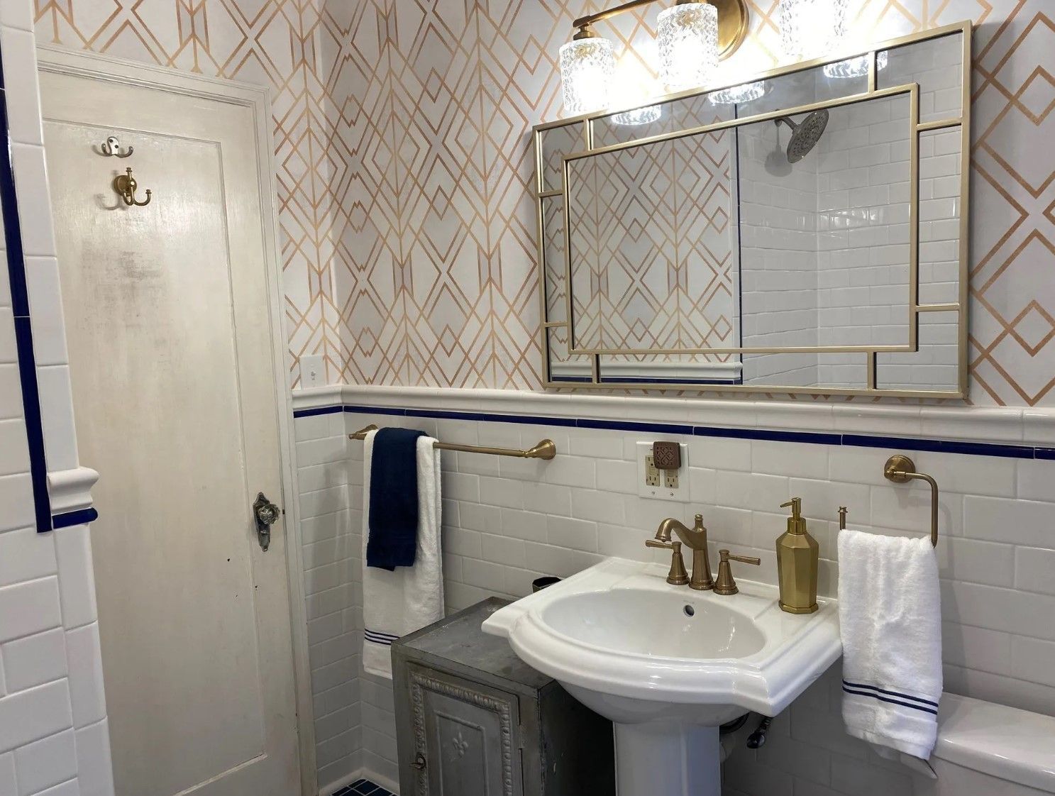 Bathroom with white and gold geometric wallpaper, pedestal sink, and gold fixtures.