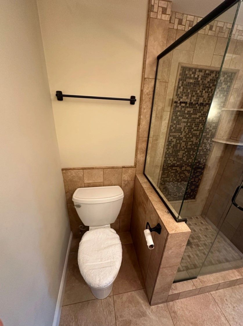 Toilet in a bathroom alcove with a glass shower door. Neutral beige color scheme.