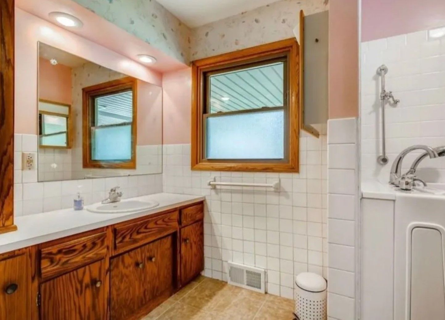 Bathroom with wood cabinets, white tiled walls, window, and sink.