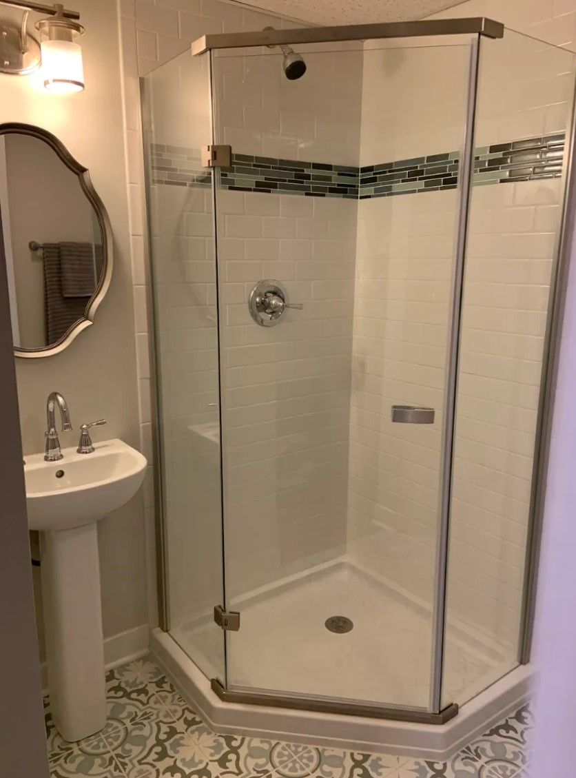 Bathroom with a hexagonal glass shower, pedestal sink, and patterned floor.
