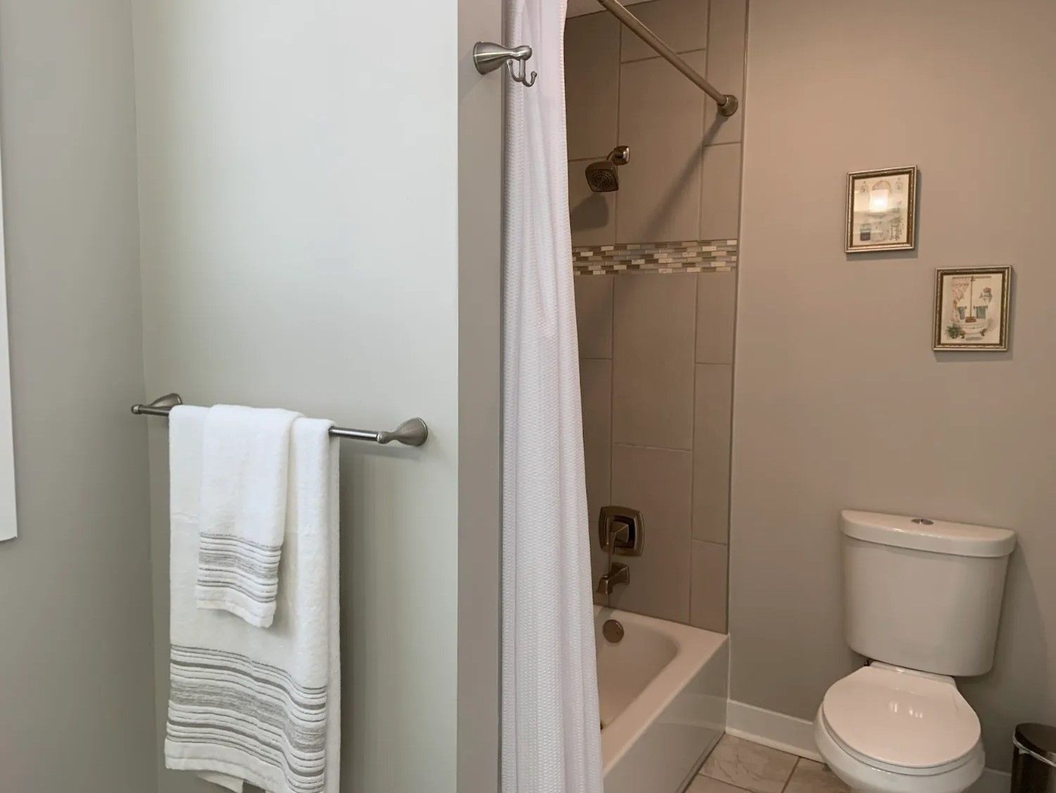 Bathroom with a white toilet, bathtub, shower, towels, and decorative framed pictures on the wall.