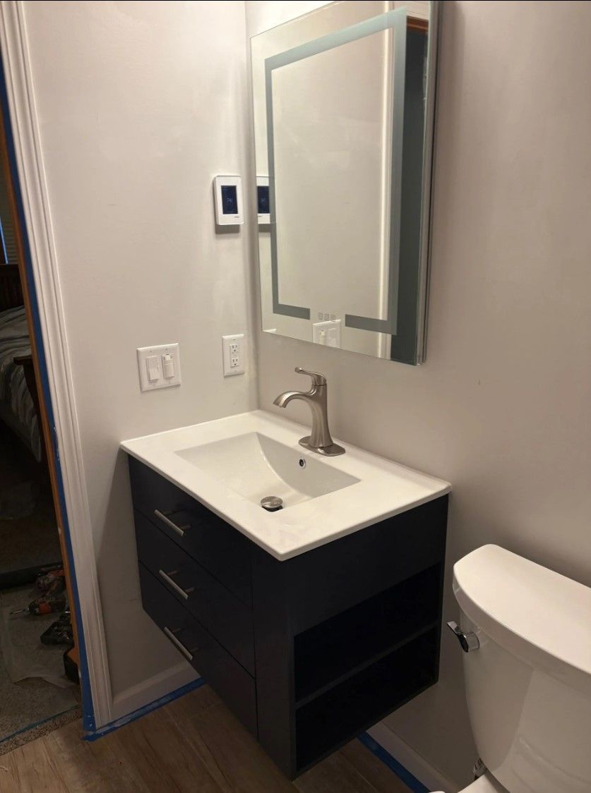 Bathroom with floating vanity, sink, mirror with lights, and a toilet.
