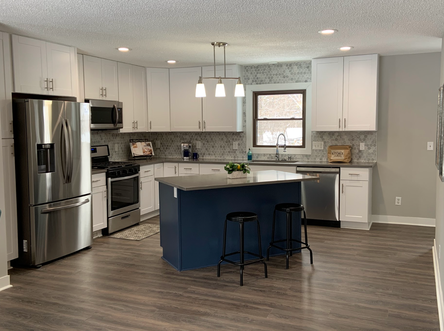 Modern kitchen with white cabinets, blue island, stainless steel appliances, and dark flooring.