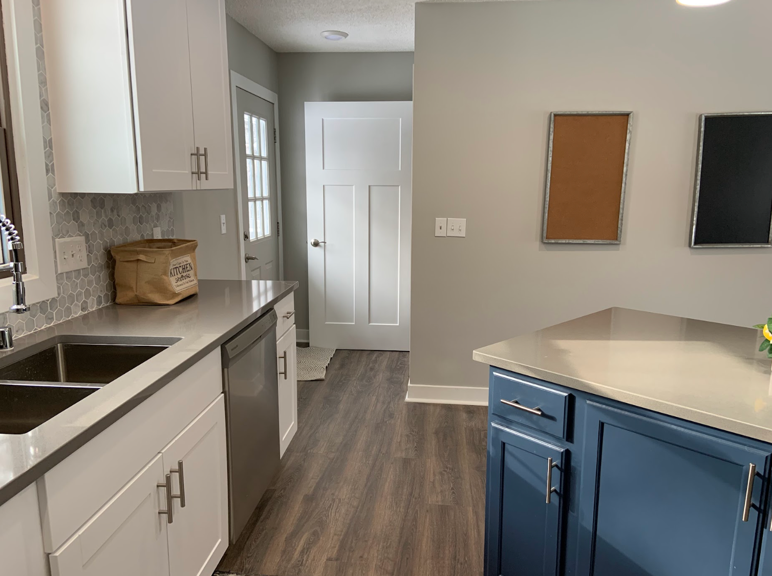 Kitchen with white cabinets, blue island, grey countertop, and wooden floor.