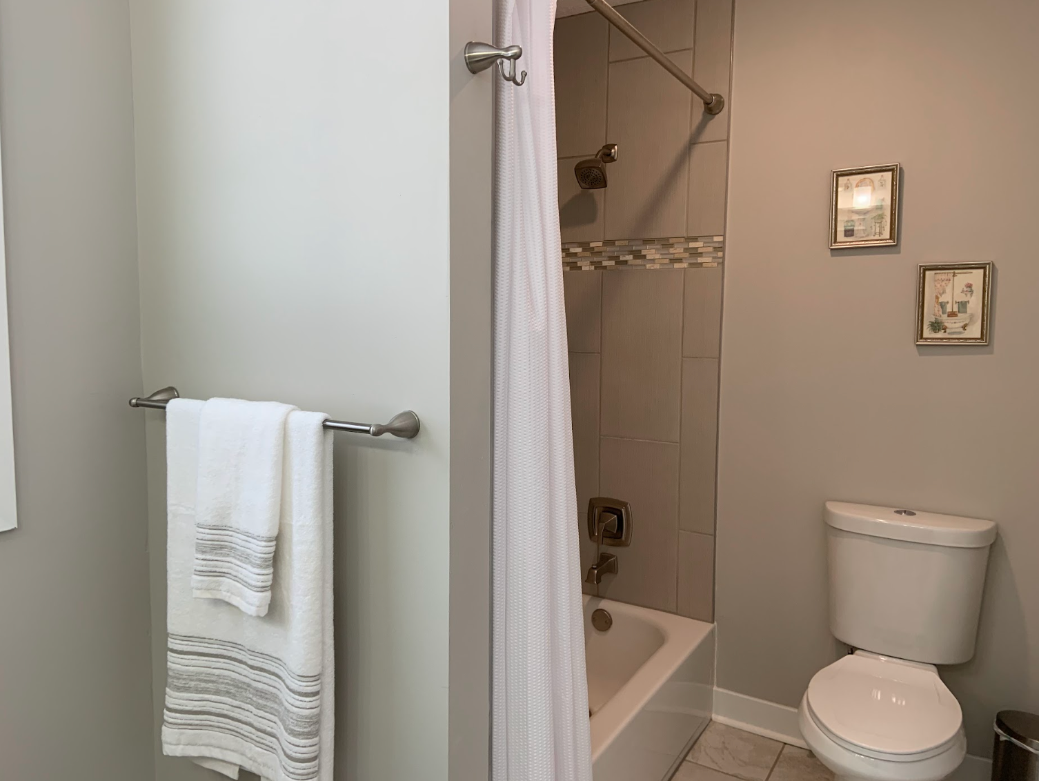 Bathroom with a white toilet, bathtub, shower, towels, and decorative framed art on the wall.