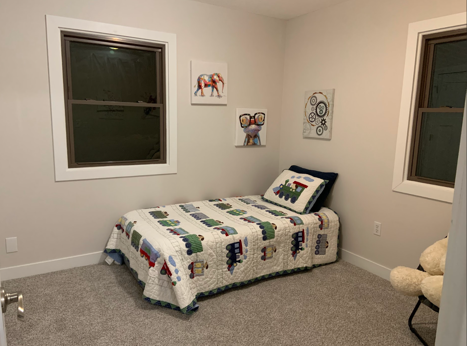 Small bedroom with bed, quilt, artwork, and two windows.