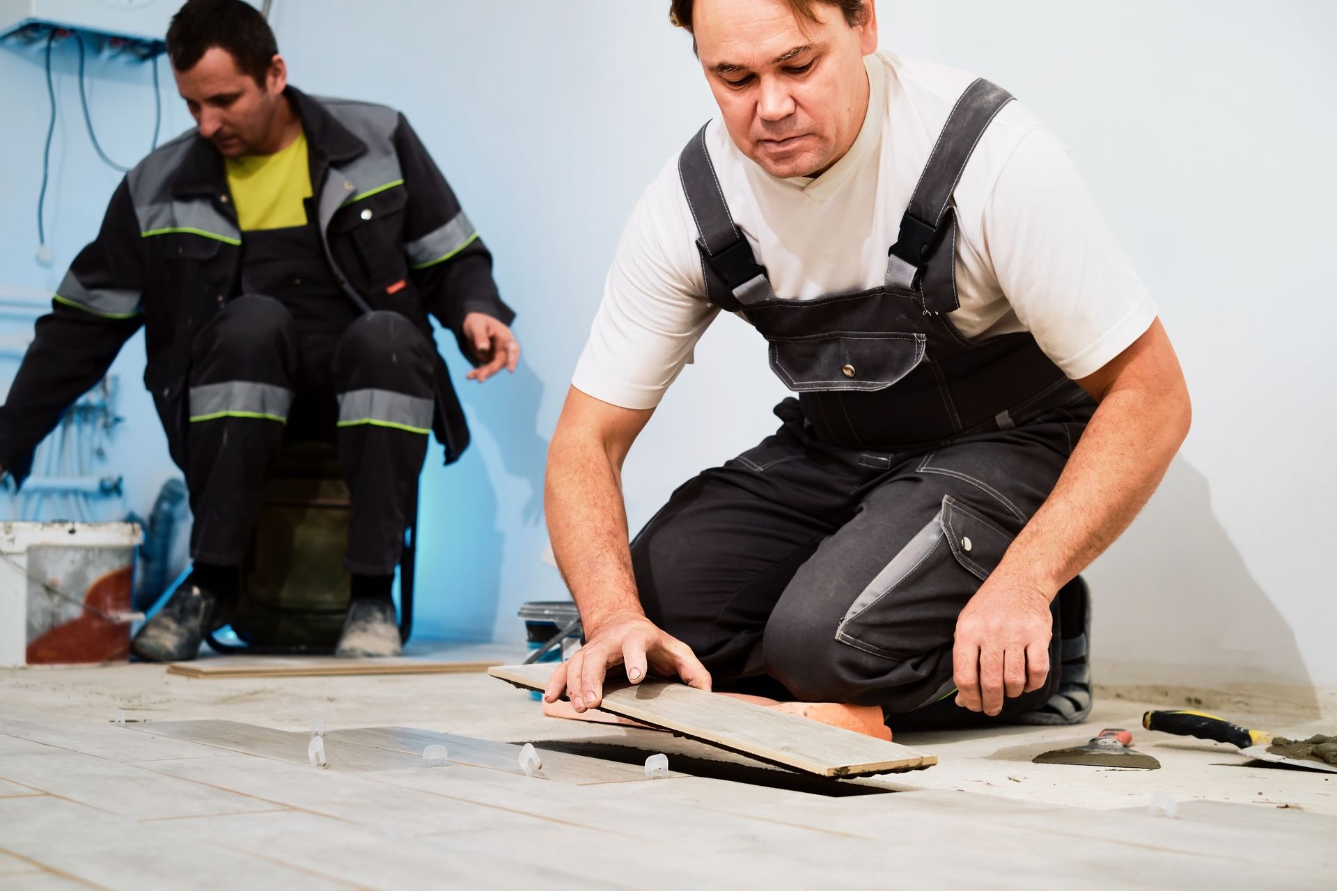 Two men are working on a tile floor.