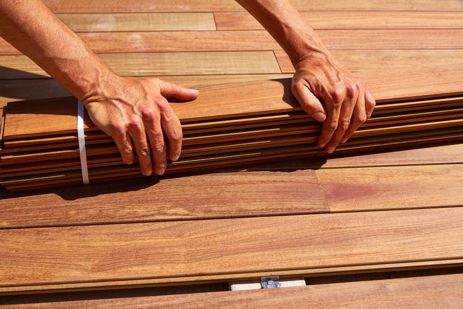 A person is holding a stack of wooden planks on a wooden deck.