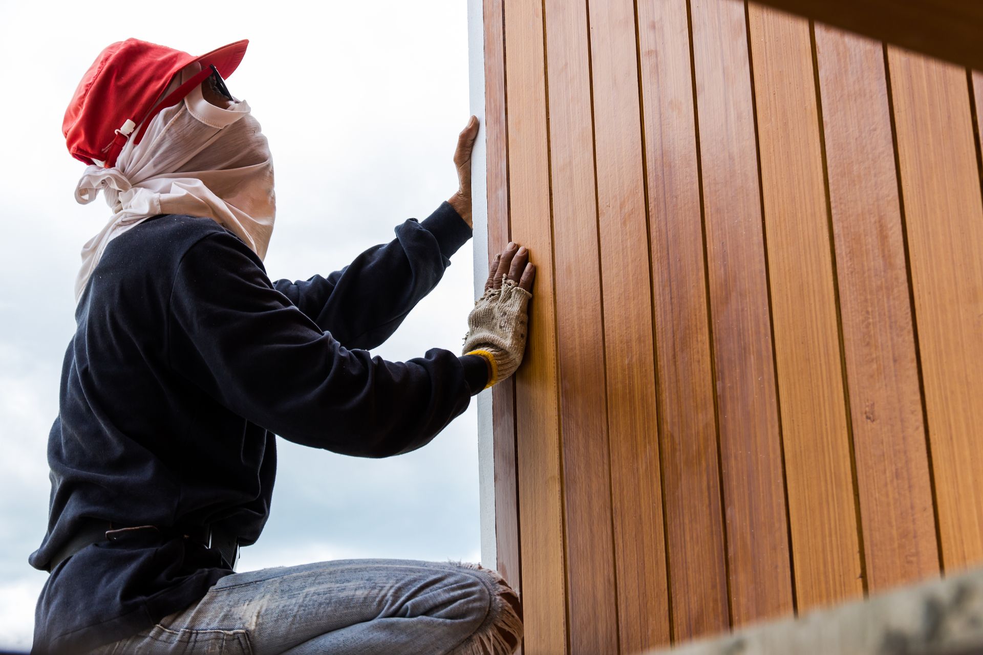 A man is kneeling down and painting a wooden wall.