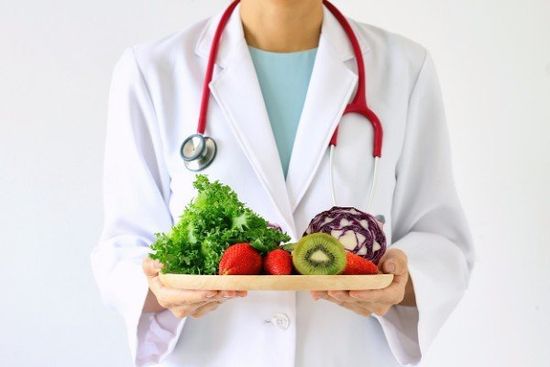 donna con camice bianco e in mano un vassoio con frutta e verdura