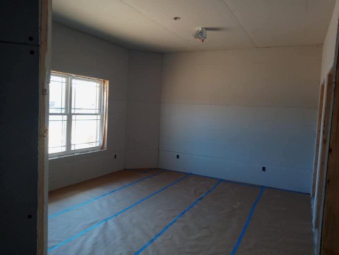 Empty room under construction with a window, unfinished walls, and protective floor covering.