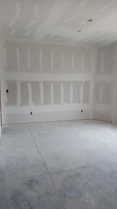 Room with unfinished drywall and concrete floor, showing studs and electrical outlets.