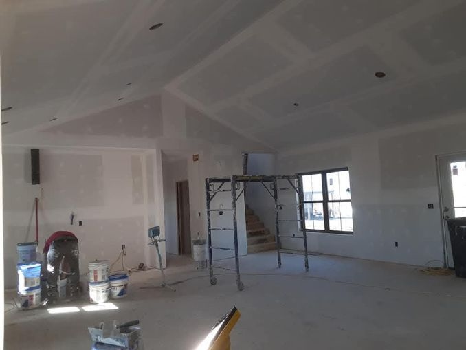 Interior of a room under construction with drywall and scaffolding, featuring a slanted ceiling and a window.