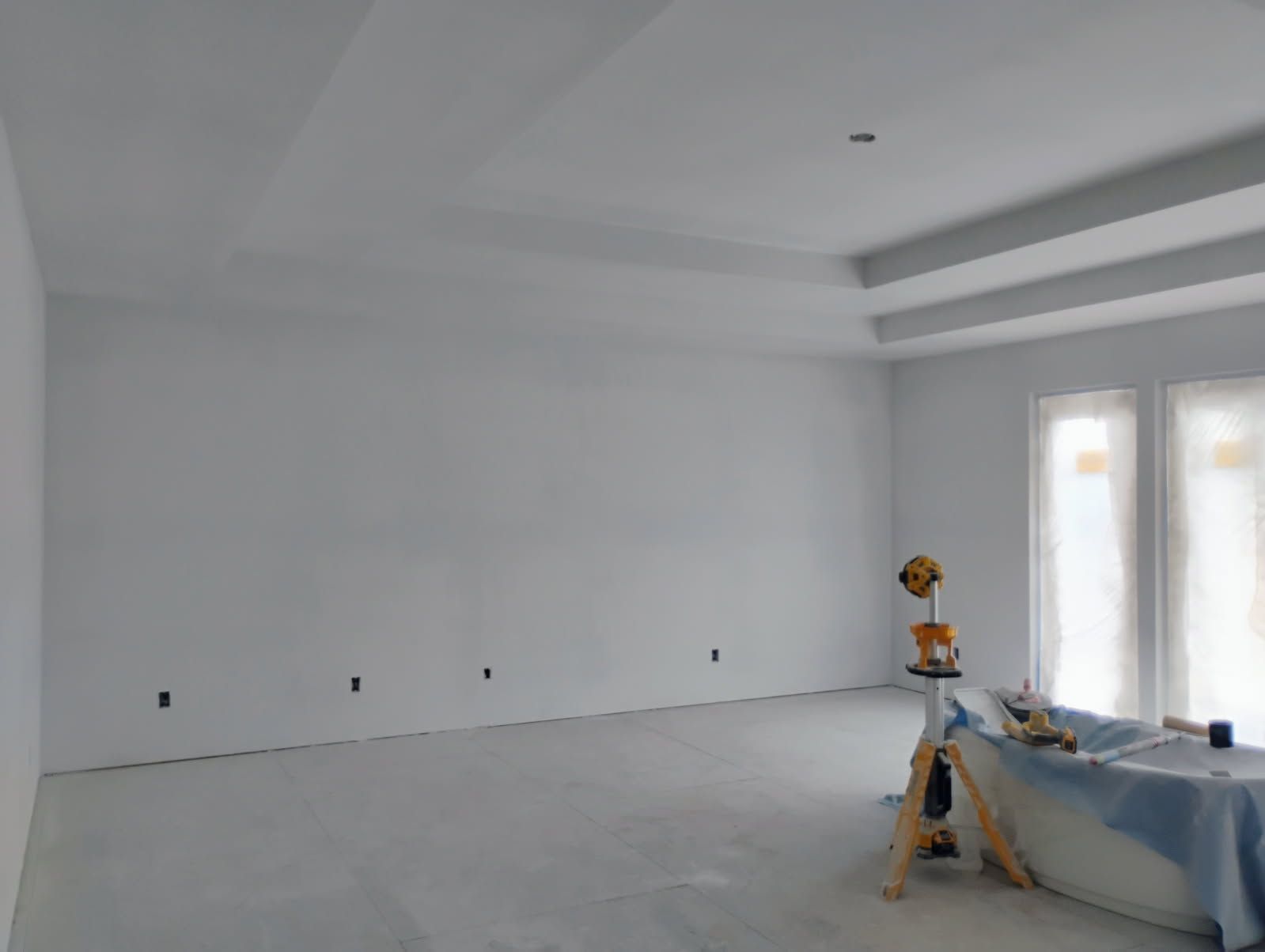 Empty white room with tray ceiling, bare walls, and unfinished flooring.