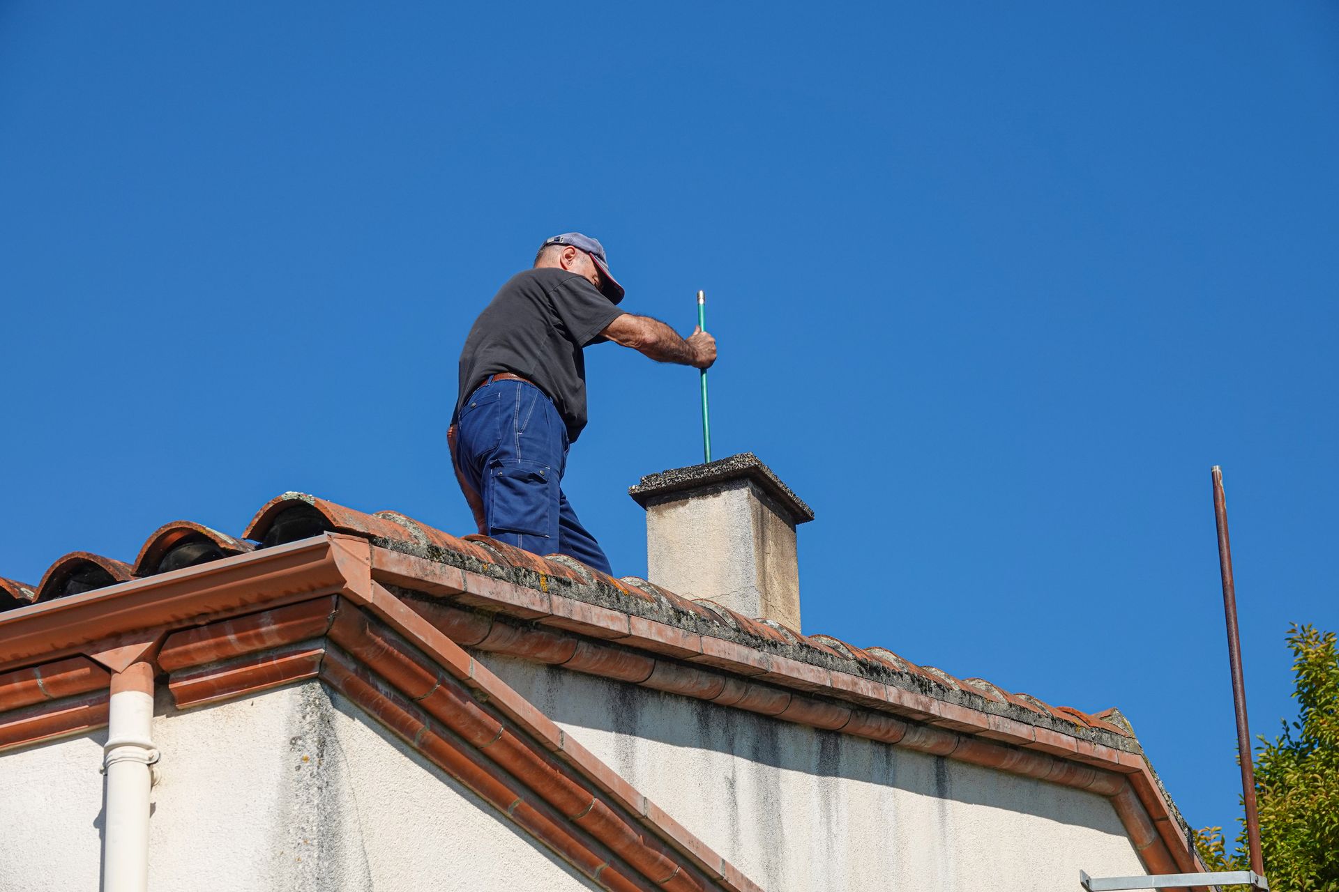 A man on a house roof, focused on chimney inspections and ensuring proper maintenance.