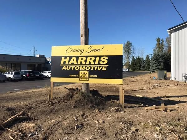 A sign for harris automotive is sitting on a pole in the dirt.
