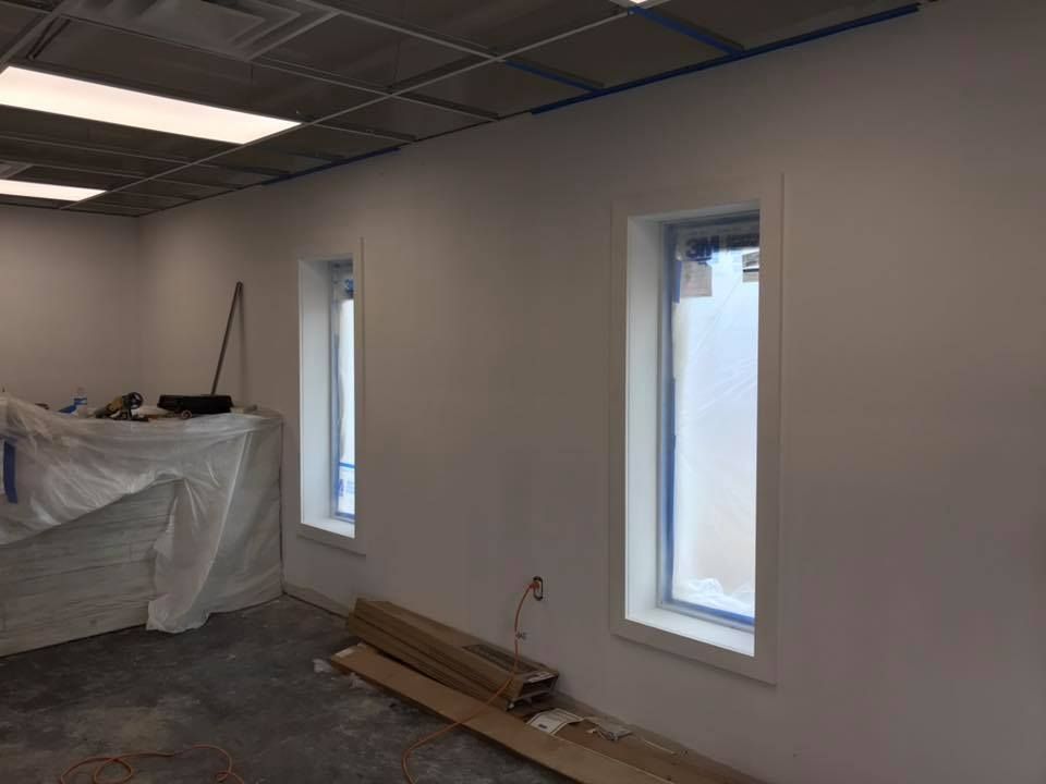 A room with two windows and a stack of wood on the floor.