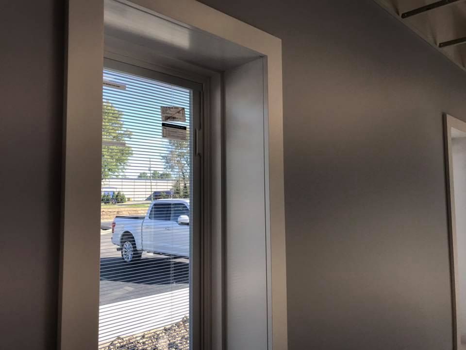 A white truck is parked in front of a window with blinds.