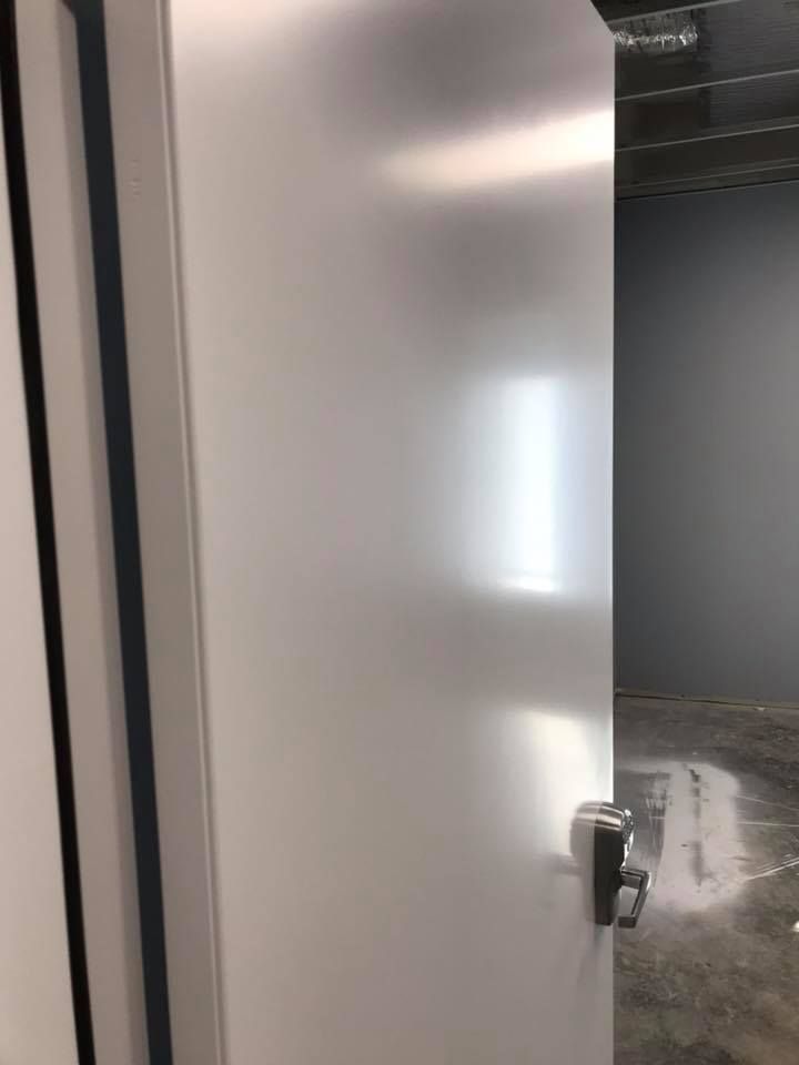 A white door with a stainless steel handle is open in an empty room.